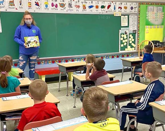 Reader at chalk board reads Tales of the Dairy Godmother to students during Ag Literacy Week.